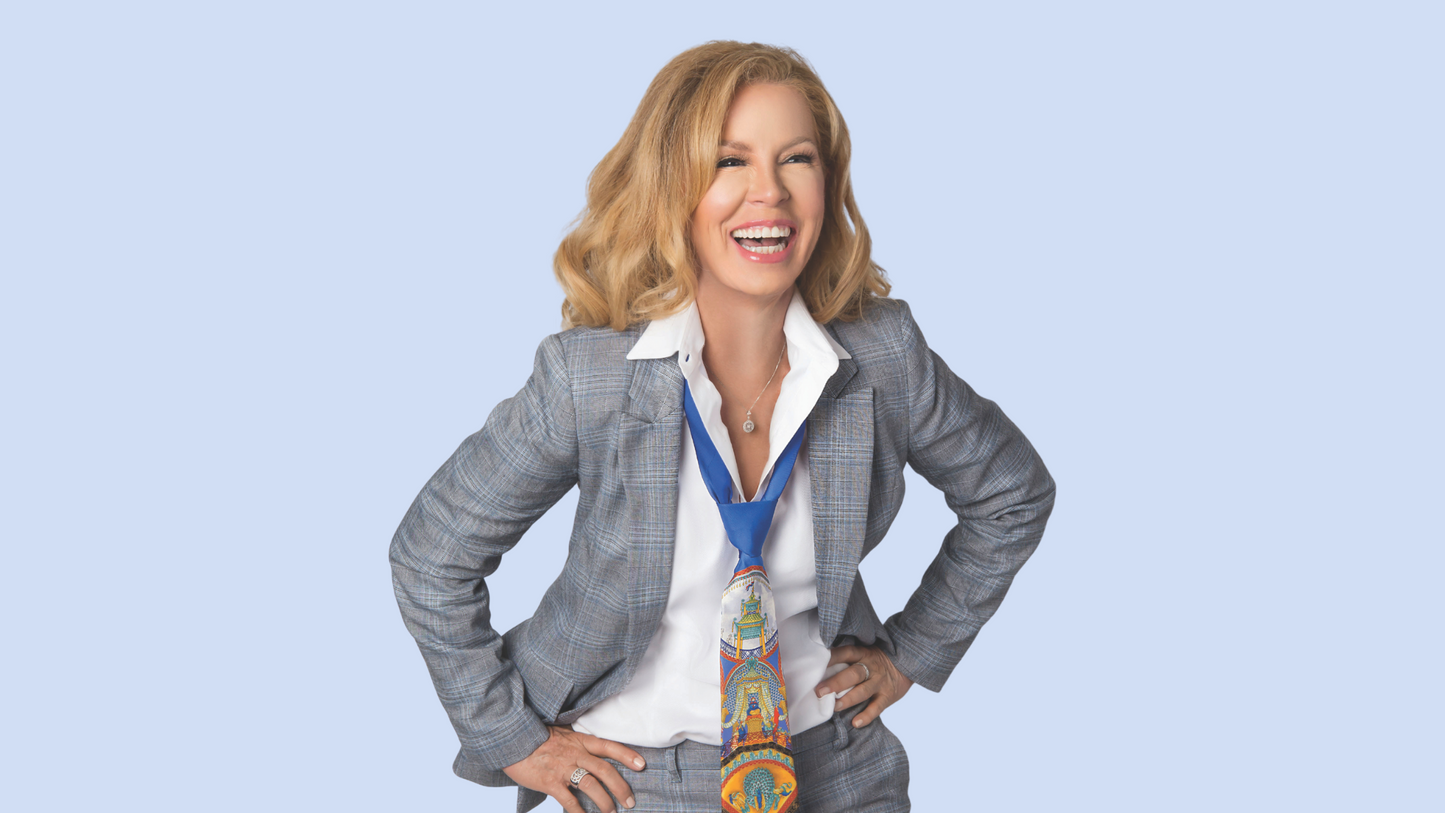 Lina laughing in a gray suite with a colorful tie on a light blue background