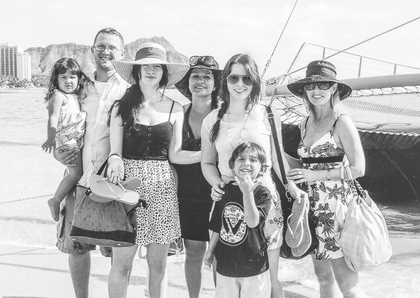 black and white photo of Lina, her kids, and grandkids posing in front of a boat at the beach in Hawaii