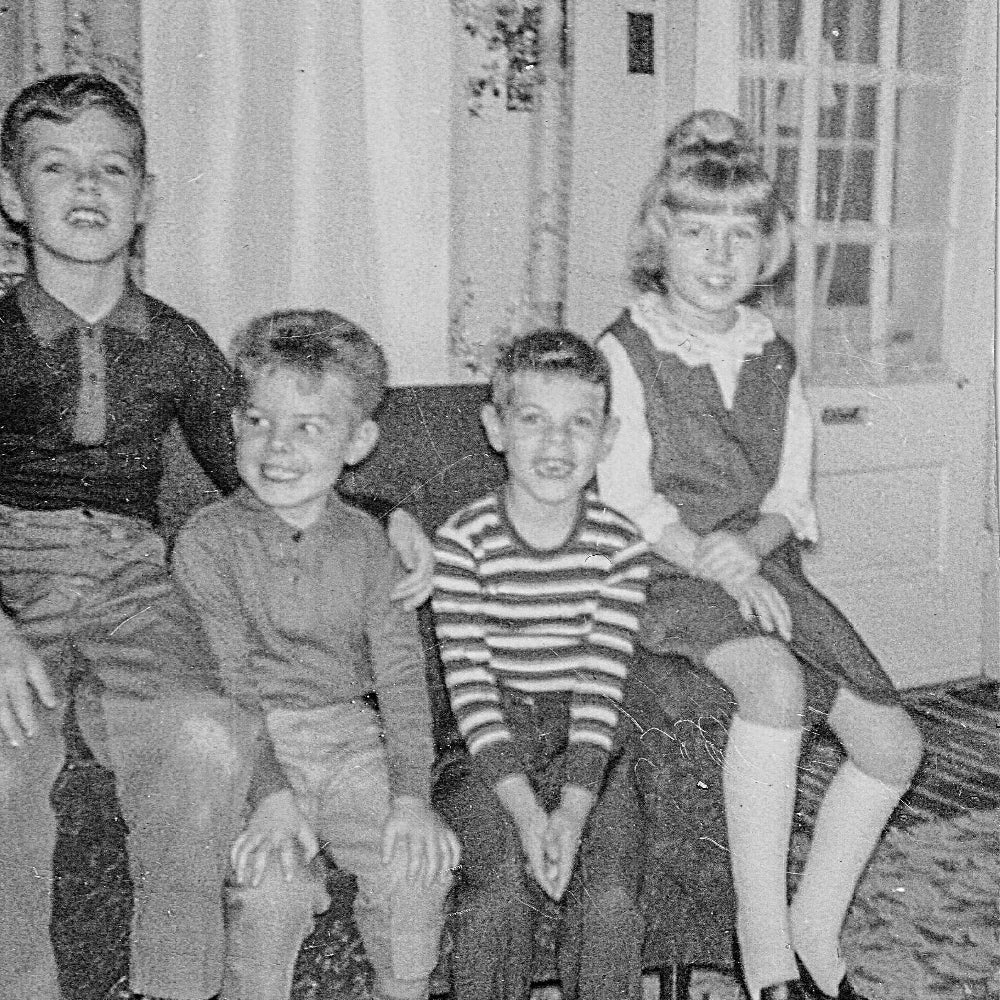 Black and white photo of a young Lina with her siblings sitting on a couch in a home setting.