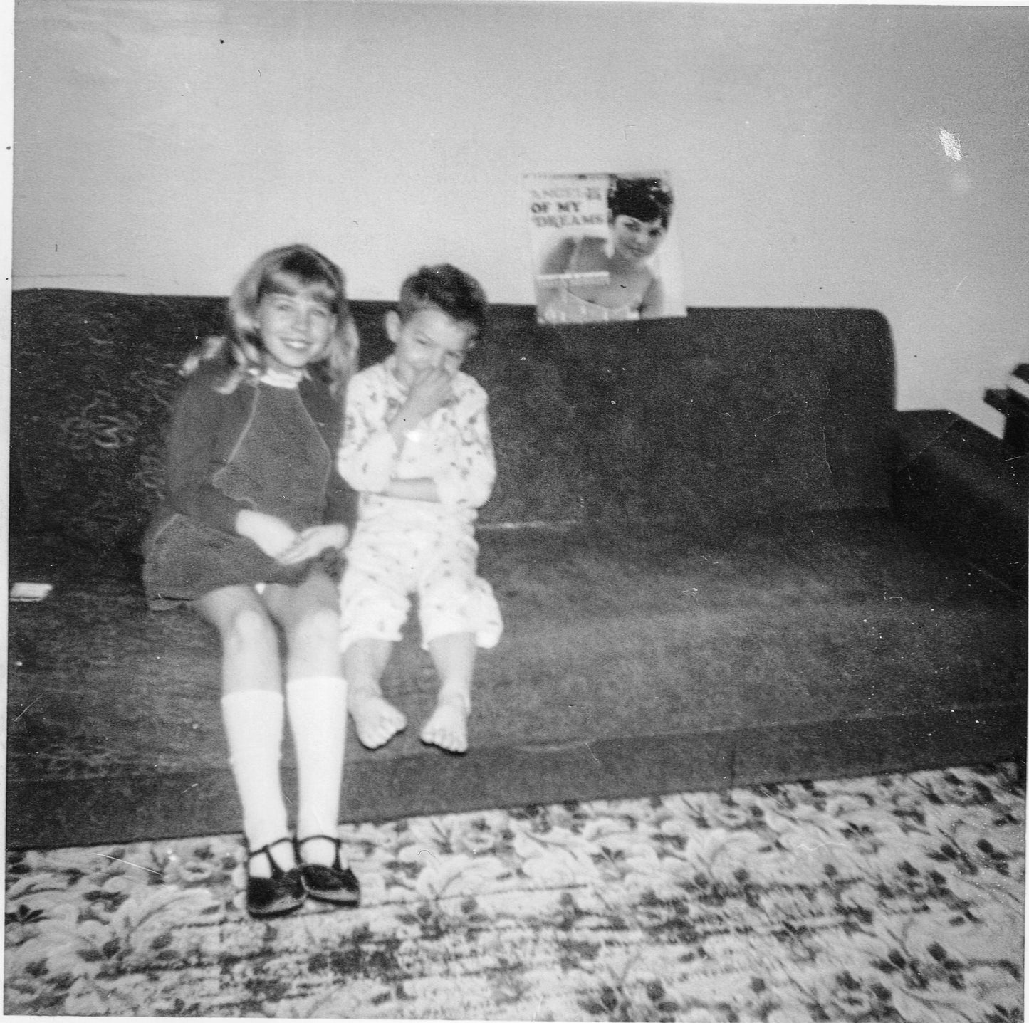 black and white image of a young Lina sitting on a couch with her younger brother